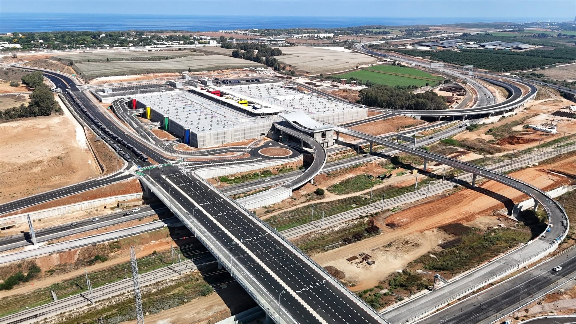 צילום אוויר של חניון רב-קומות ומחלף כבישים בשפיים, עם קו החוף והים ברקע