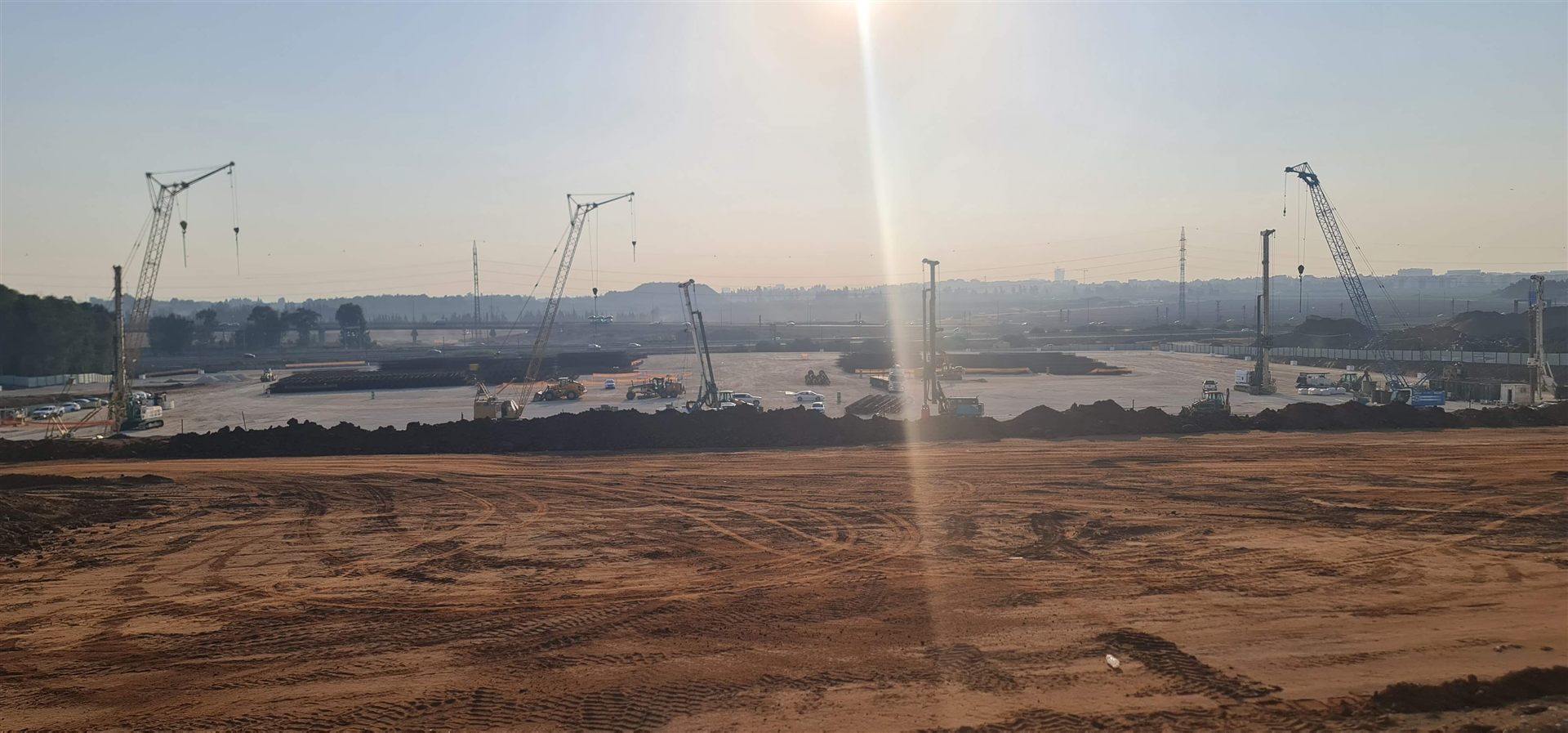 מבט רחב על אתר עבודות עפר וביסוס עם מספר עגורנים ומכונות קידוח, בשעת שחר