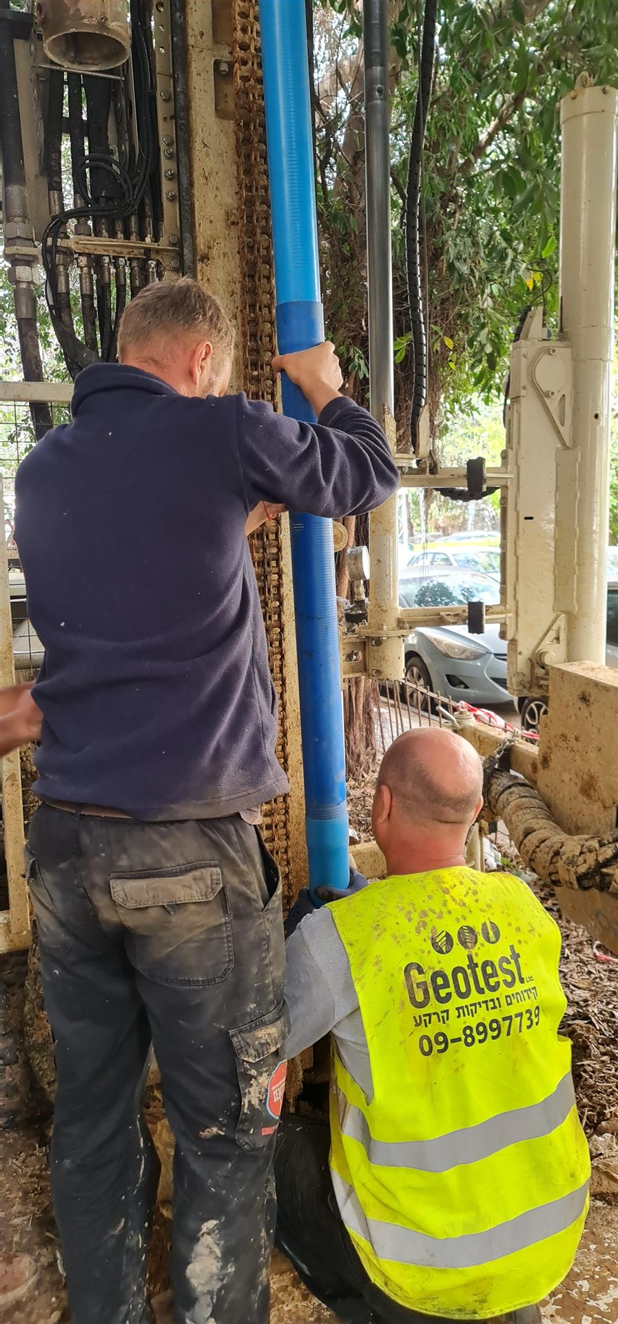 שני עובדים מתקינים צינור פיזומטר כחול במכונת קידוח, לצורך ניטור מי תהום
